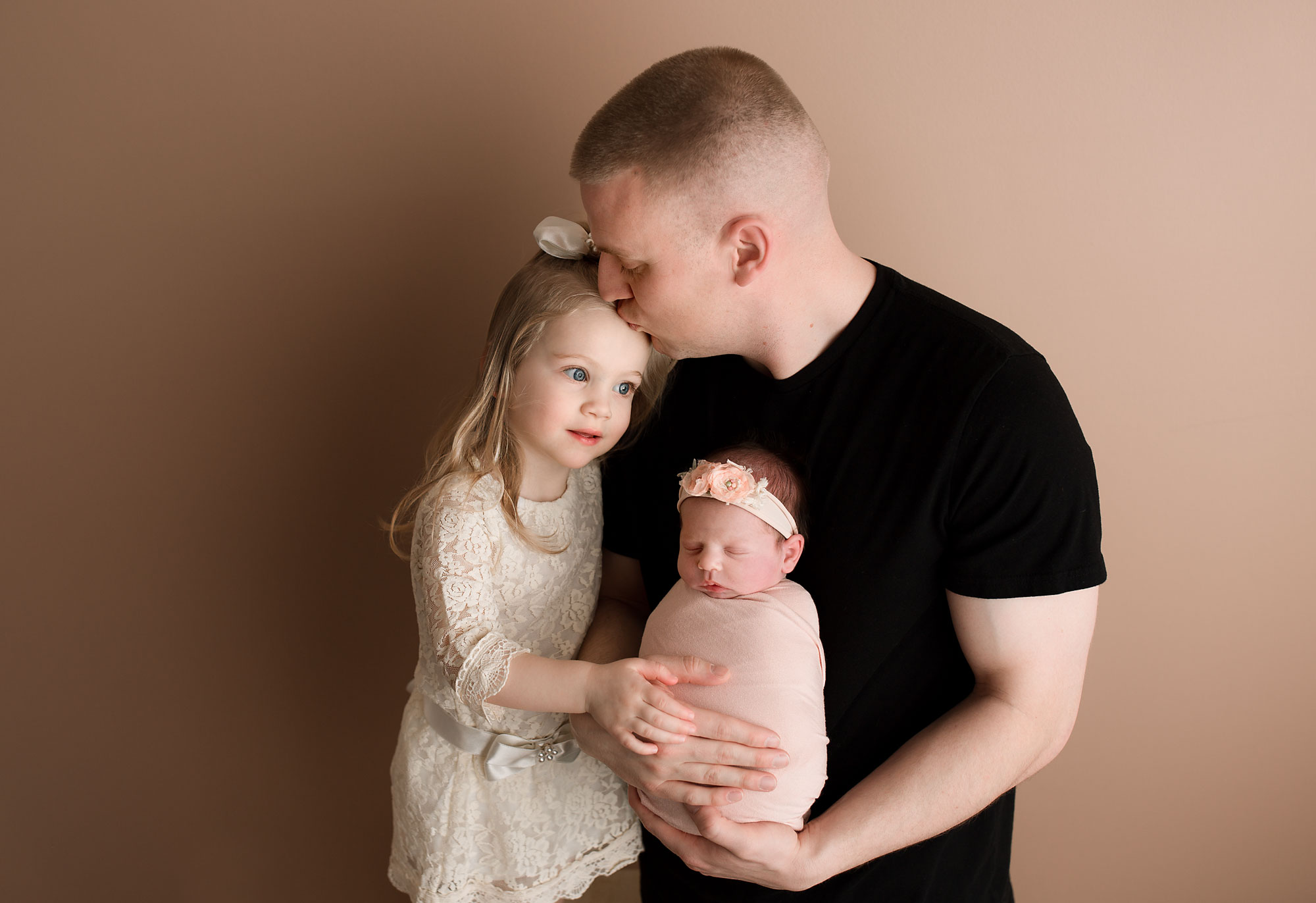 father and 2 baby girls photo, dad kissing an older daughter and holding the little baby swaddled in his arms. Morris county NJ newborn photographer , Yellow Lollipop Photography