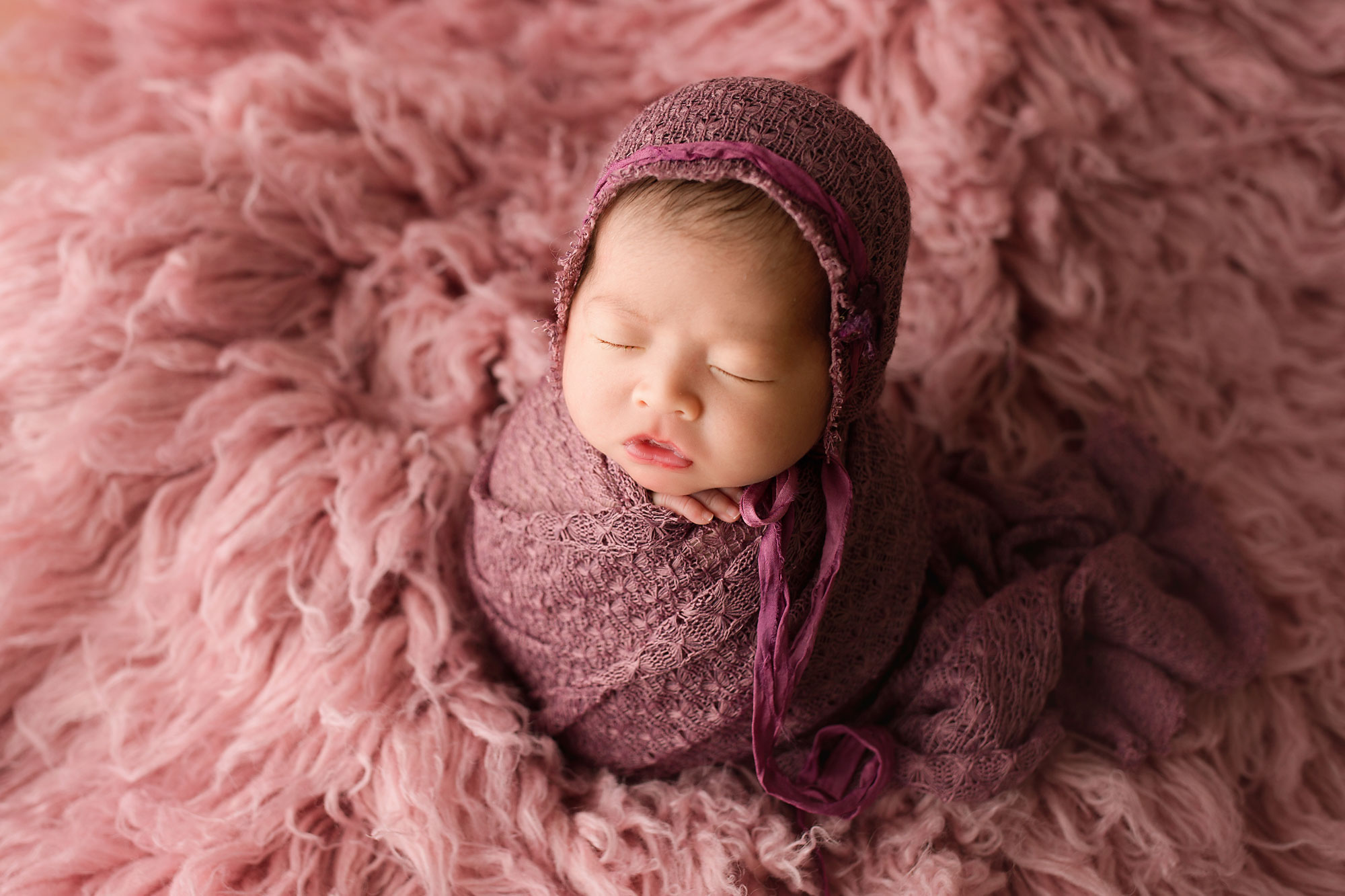 swaddled baby girl on a pink rug, potato pose 