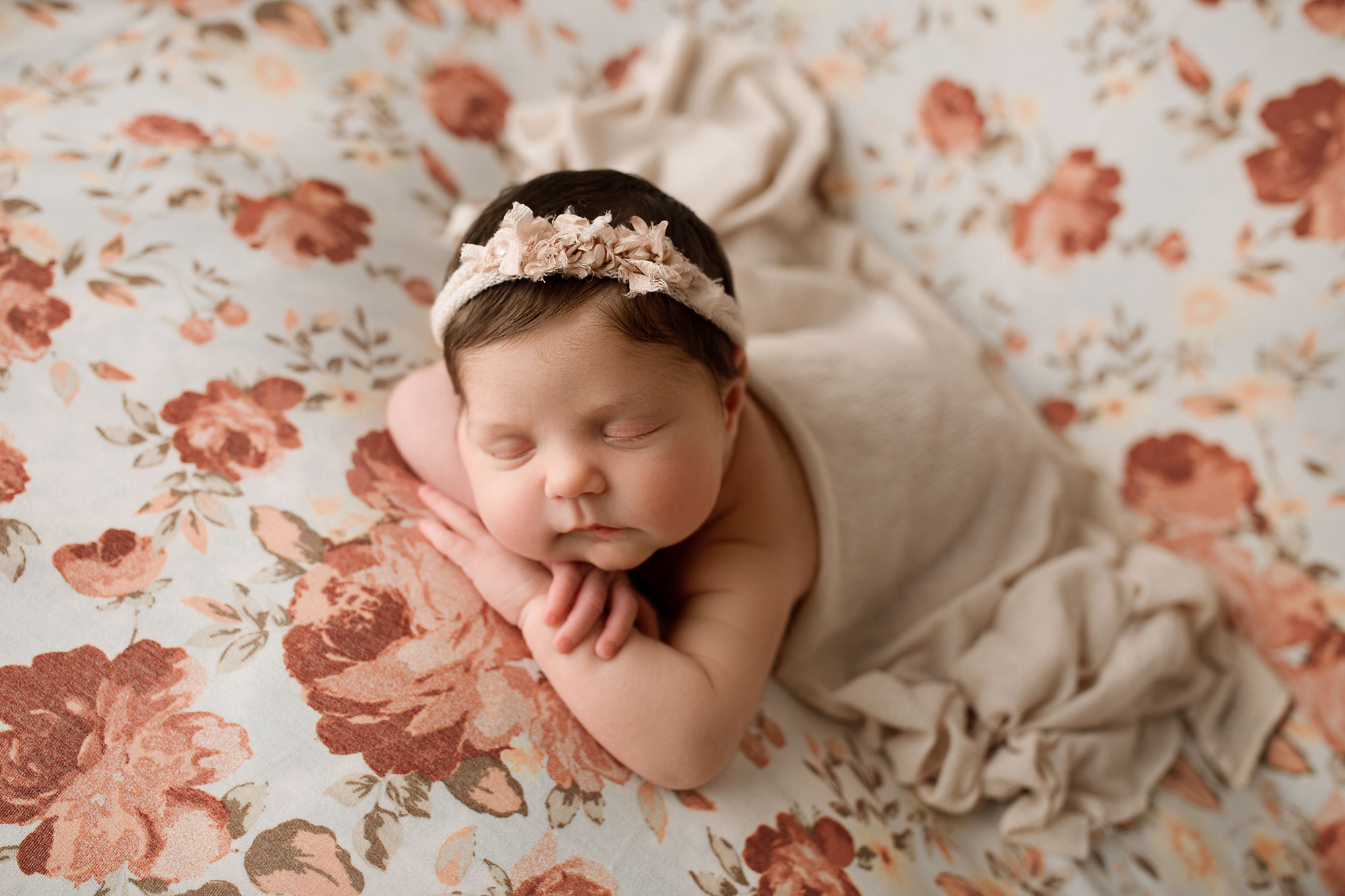newborn baby sleeping on a floral backdrop, beanbag posing, head on hands pose, neutral set up