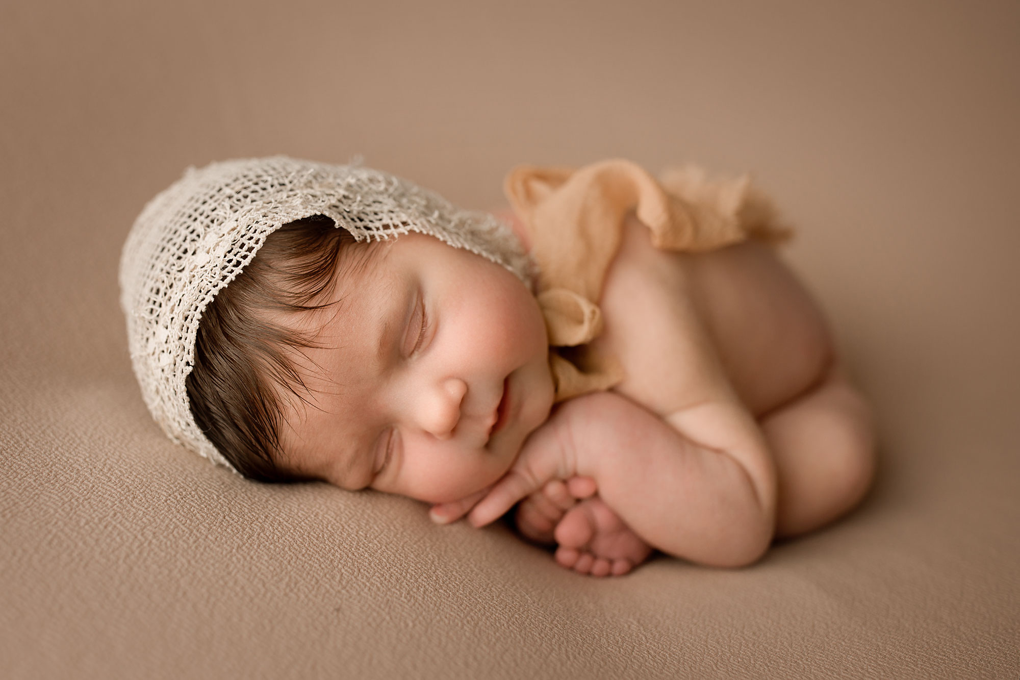 newborn baby girl posing, baby sleeping on a beige blanket, taco pose, bonnet 