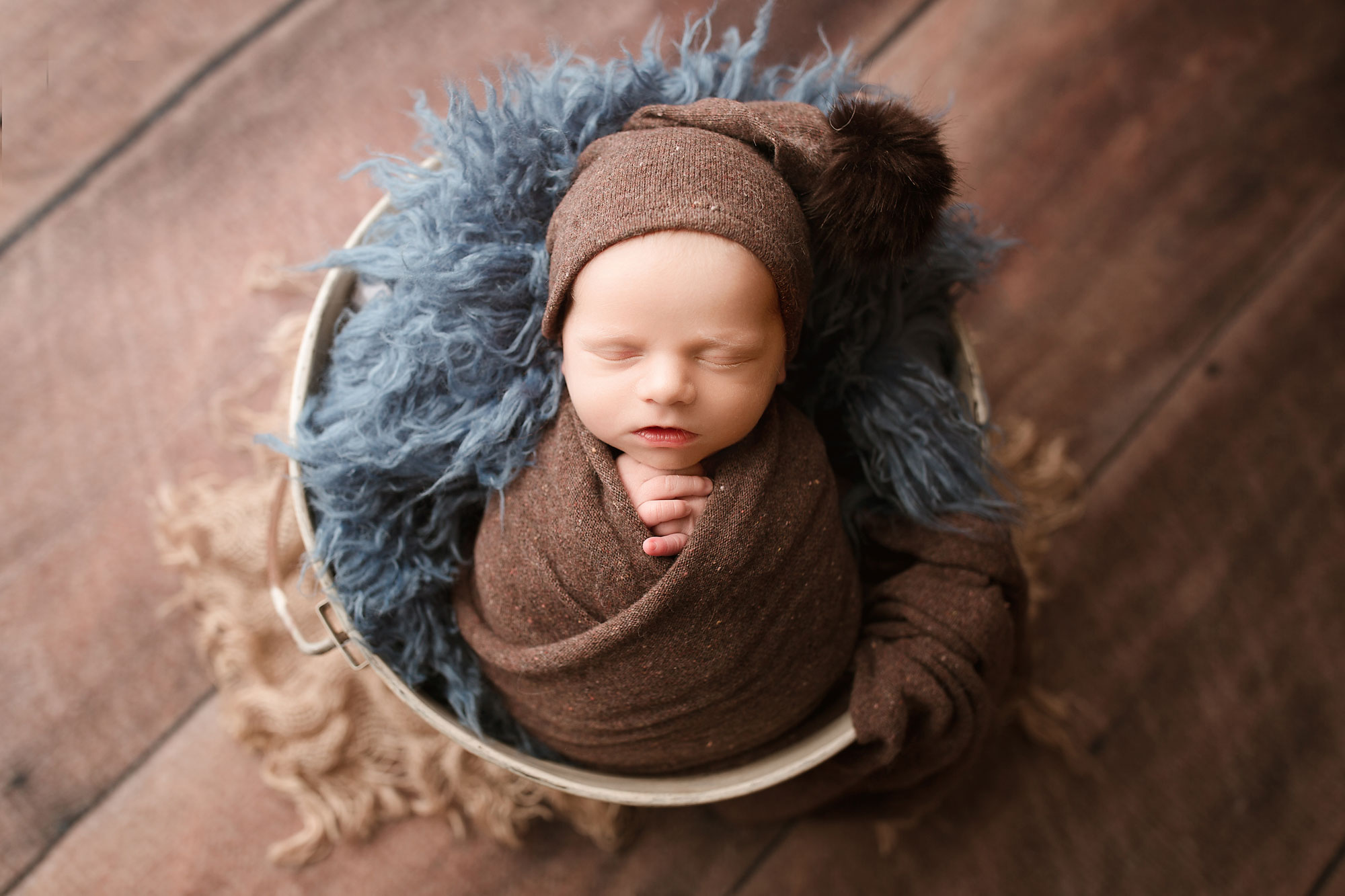 newborn pictures near me, swaddled baby asleep in bucket with blue and brown furs
