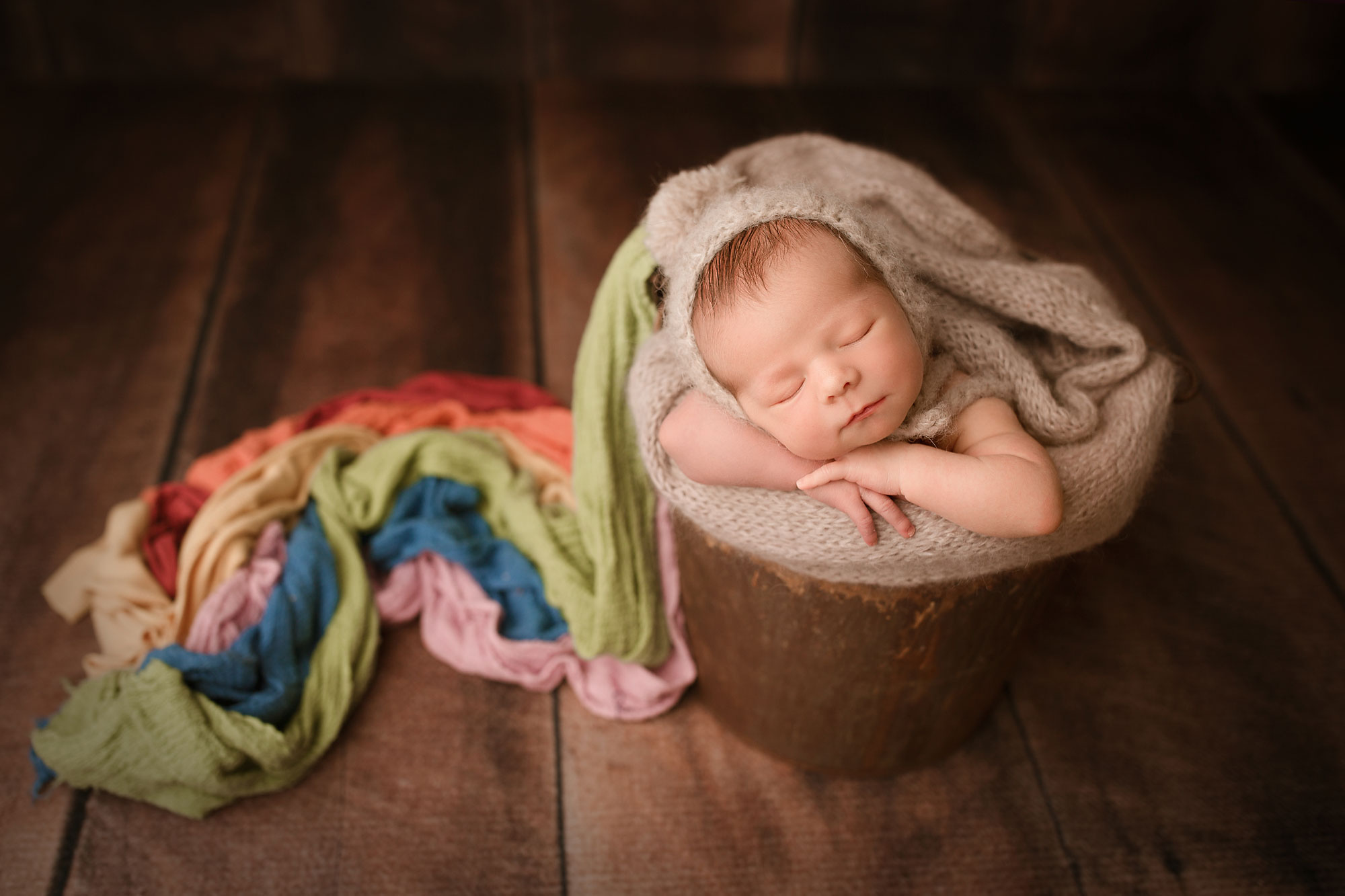 rainbow baby photographer near me, baby sleeping in rustic bucket with rainbow blanket draped across wooden background