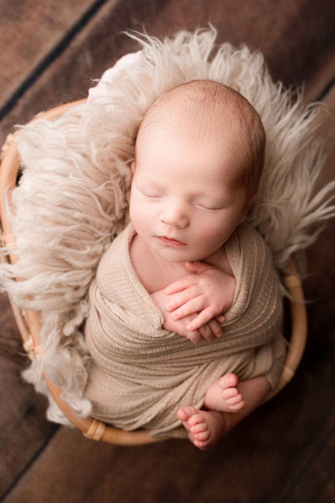 newborn photography session flemington nj, swaddled baby asleep in basket with cream colored fur against wood floor background