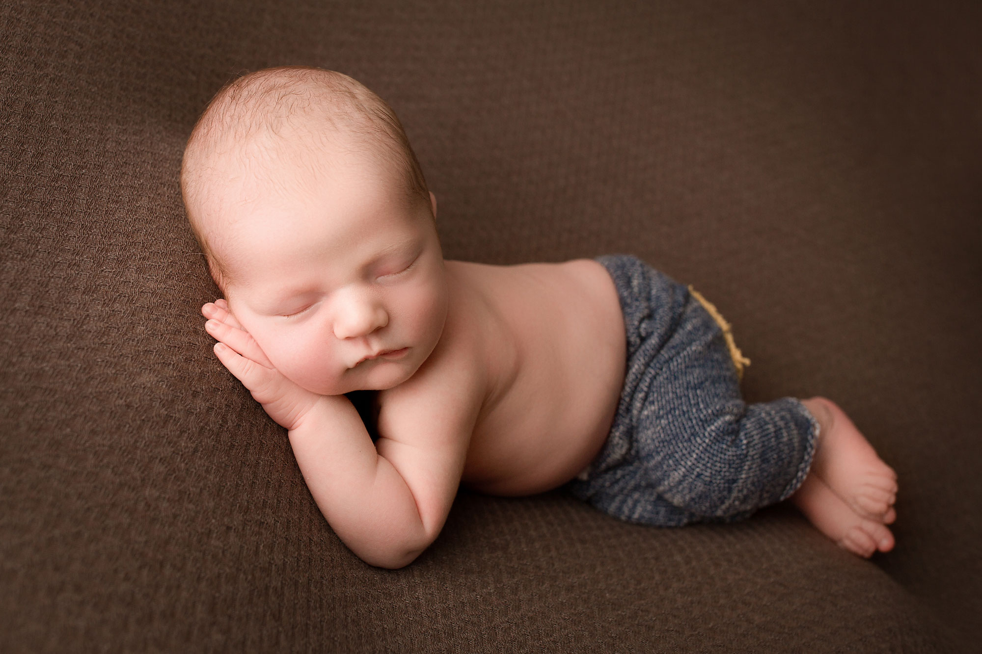 newborn photography near me new jersey, sleeping baby boy in blue pants against brown background