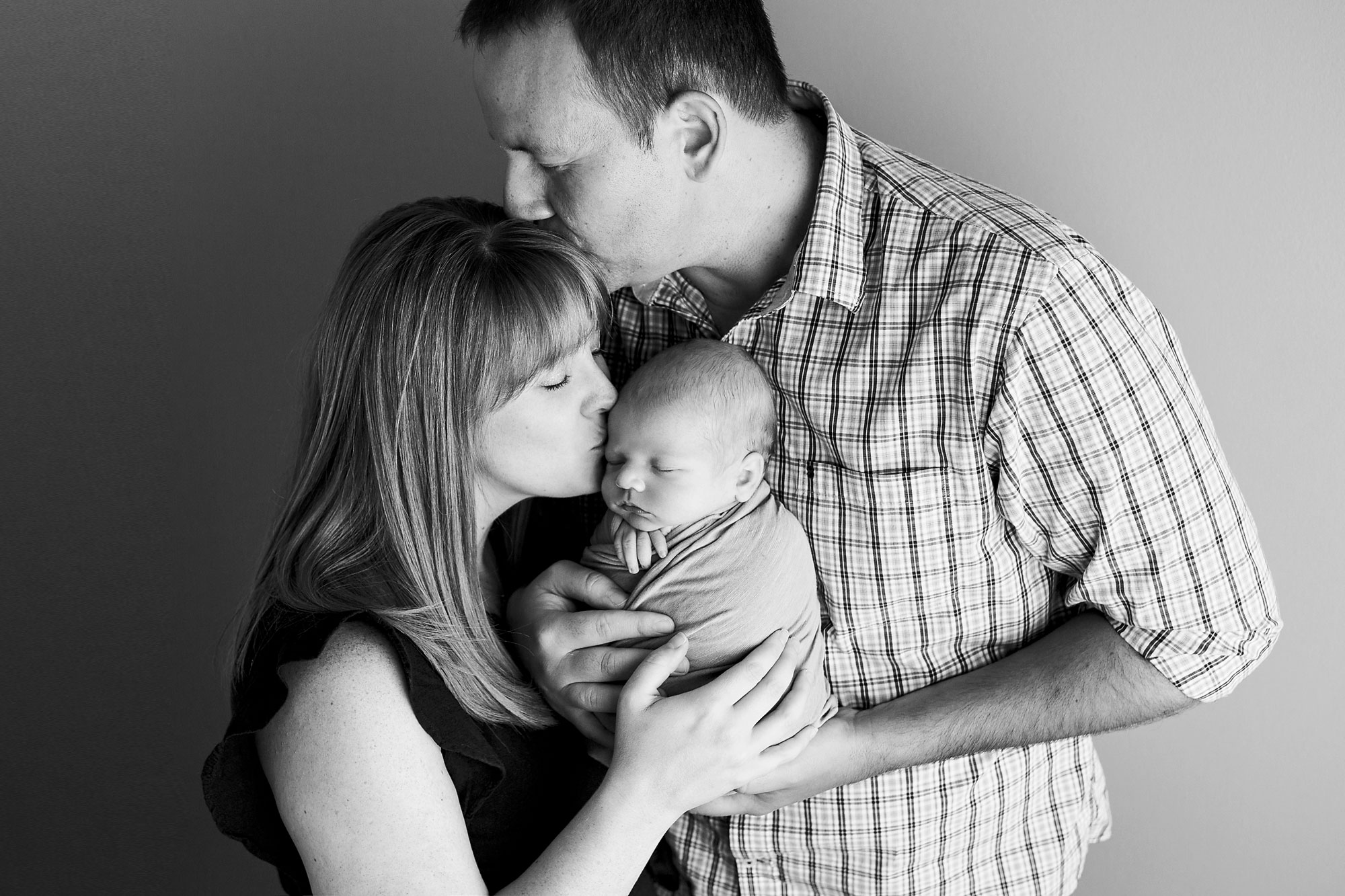 newborn and family photos, black and white image of family with dad kissing mom and mom kissing new baby boy