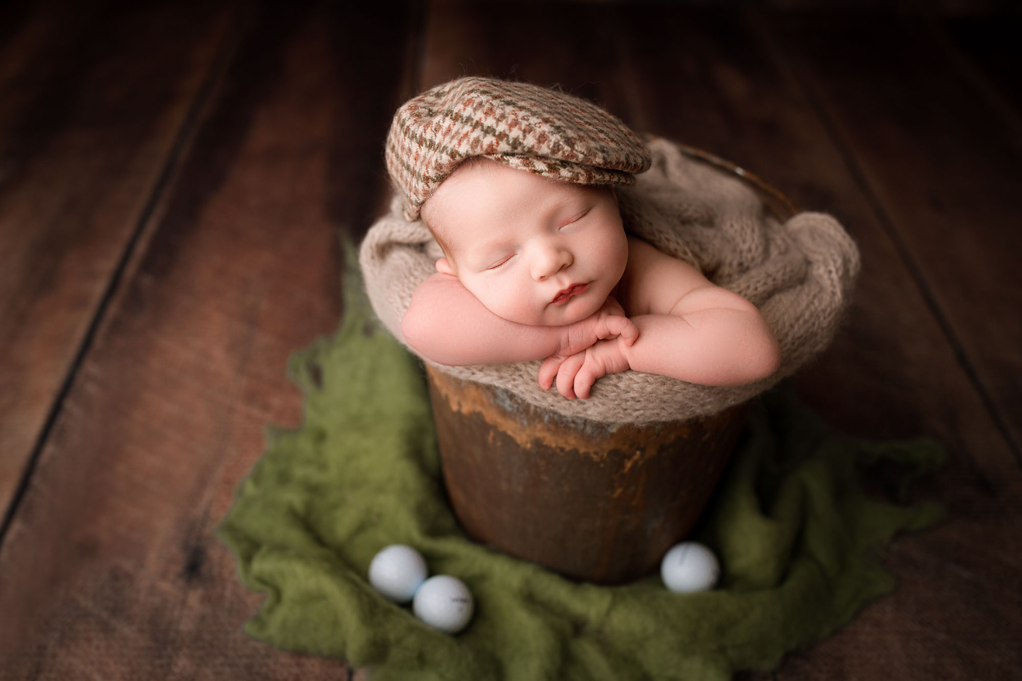 newborn photography session flemington nj, baby boy asleep in rustic bucket wearing flat cap with golf balls next to him