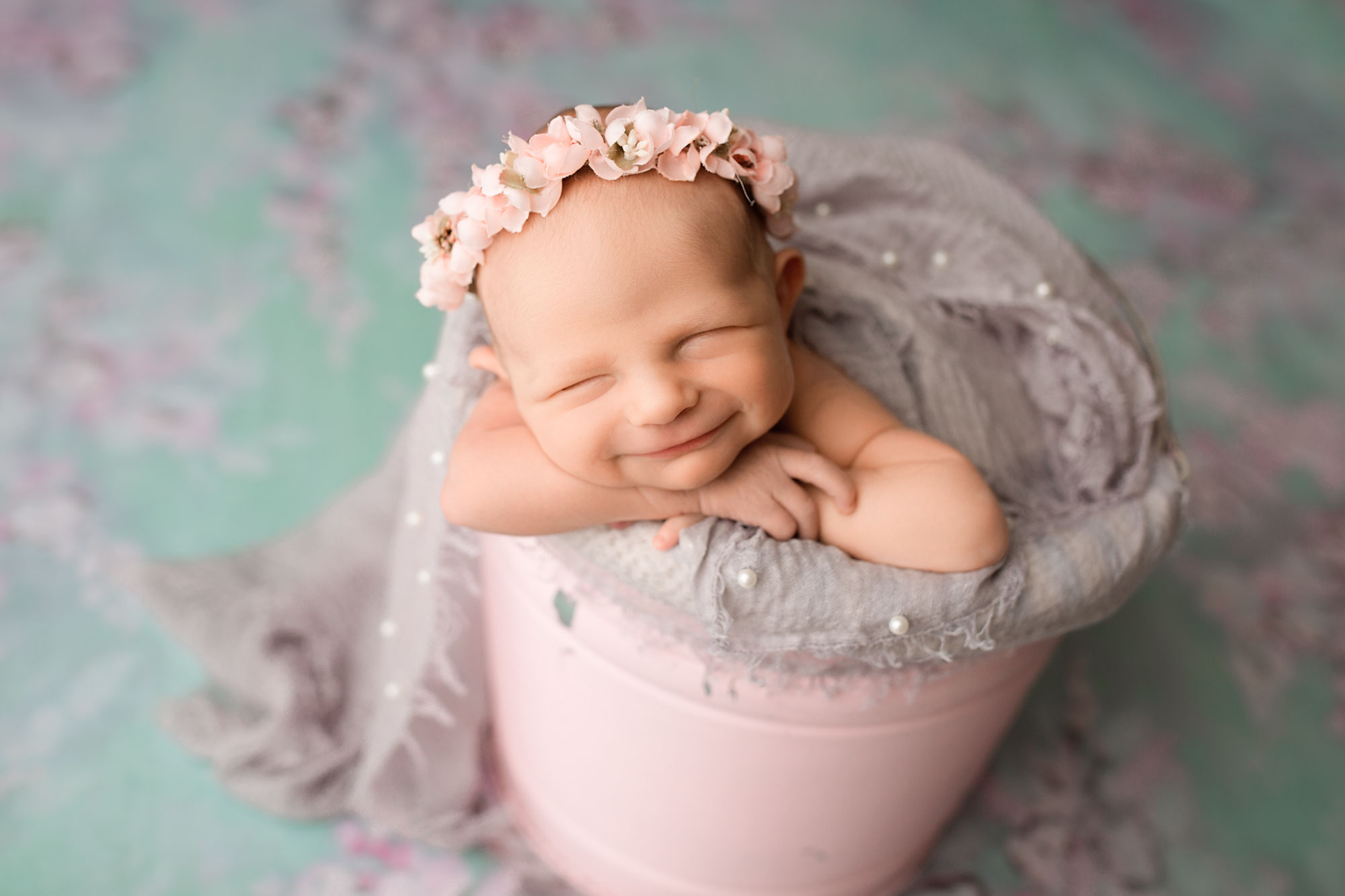 newborn photography session morris county nj, smiling baby girl asleep in pink bucket with lavender wrap and floral headband