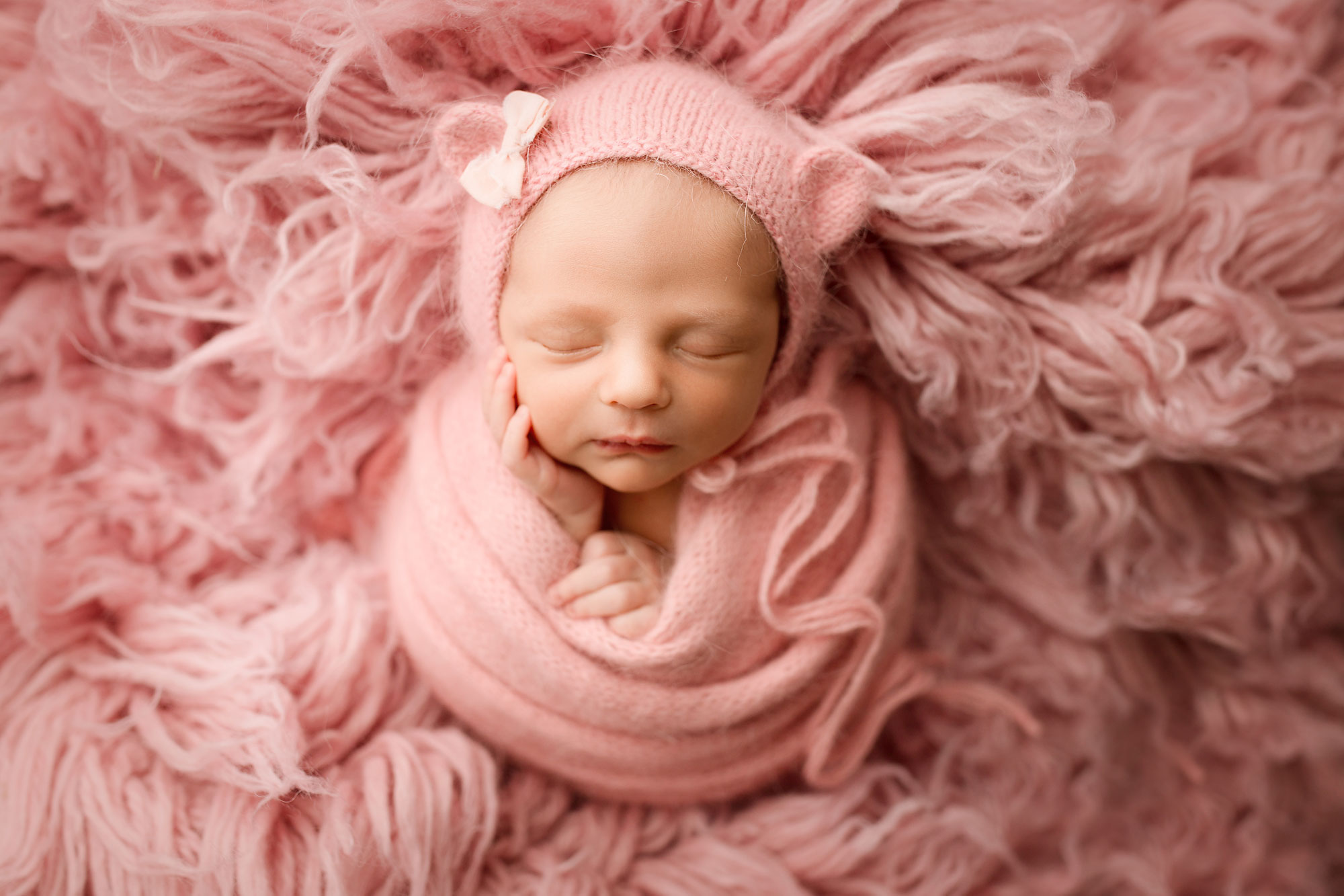 baby girl newborn photography, baby in pink swaddle and hat against pink fur background