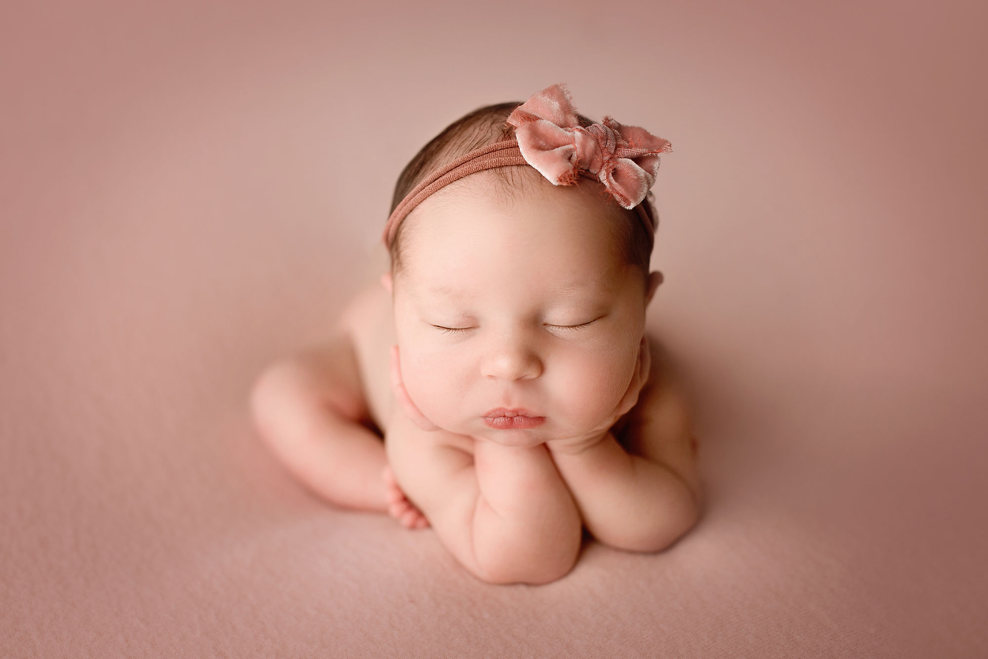 professional newborn photography near middlesex nj, baby girl asleep with chin propped in hands against a pink background