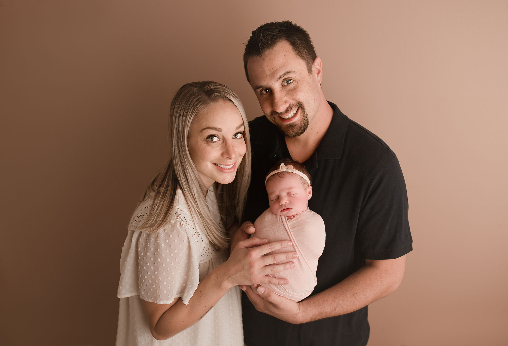 new jersey baby and family photos, mom and dad smiling while holding swaddled baby girl