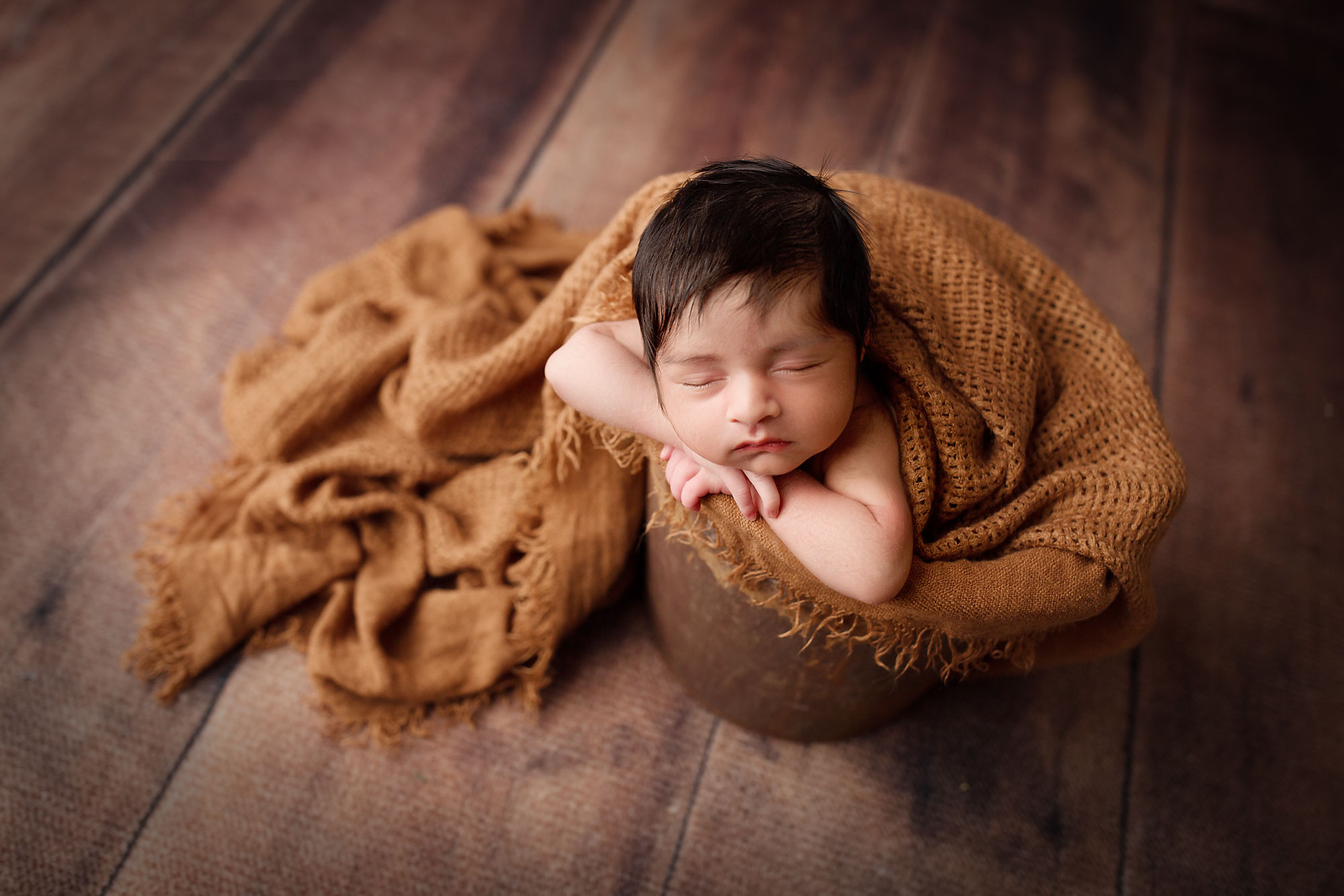 professional newborn photography near me, baby boy asleep in rustic bucket with wheat gold wrap against wooden floorboards