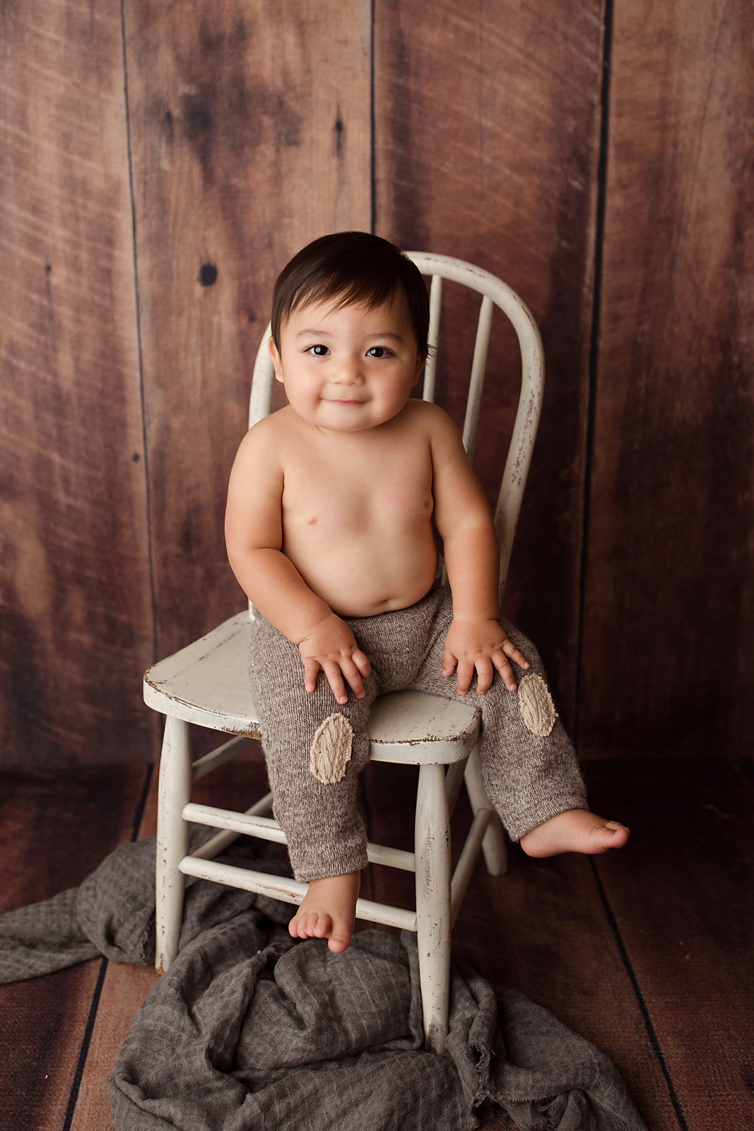 baby photo session union county nj, toddler boy in patched pants on antique chair against wood plank backdrop