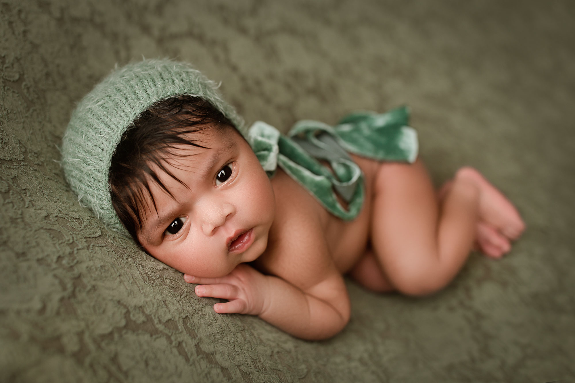 newborn photographer near me nj, wakeful baby looking at camera with green cap and ribbon