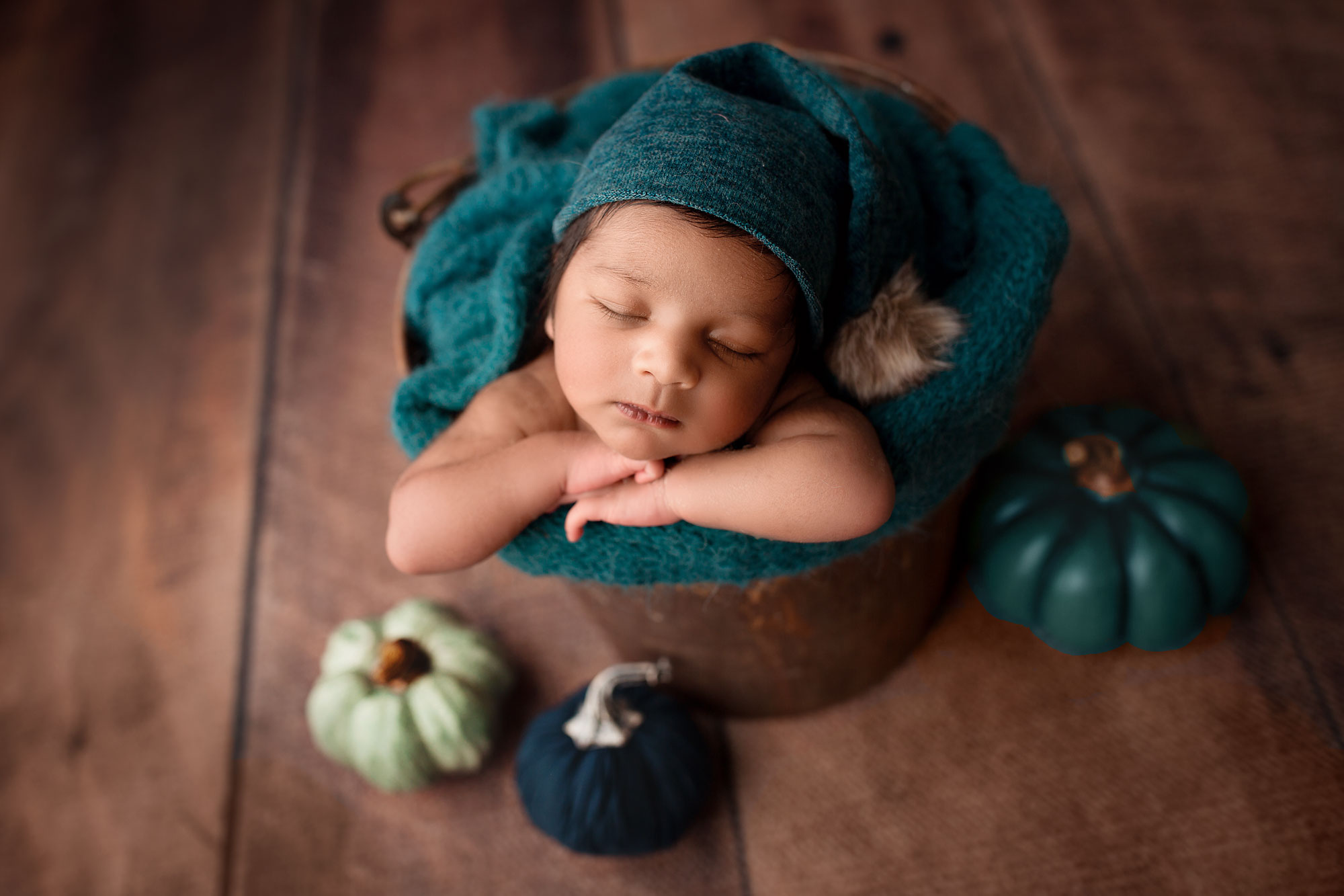 professional newborn photos near me, baby asleep in bucket with blue cap and blue pumpkins
