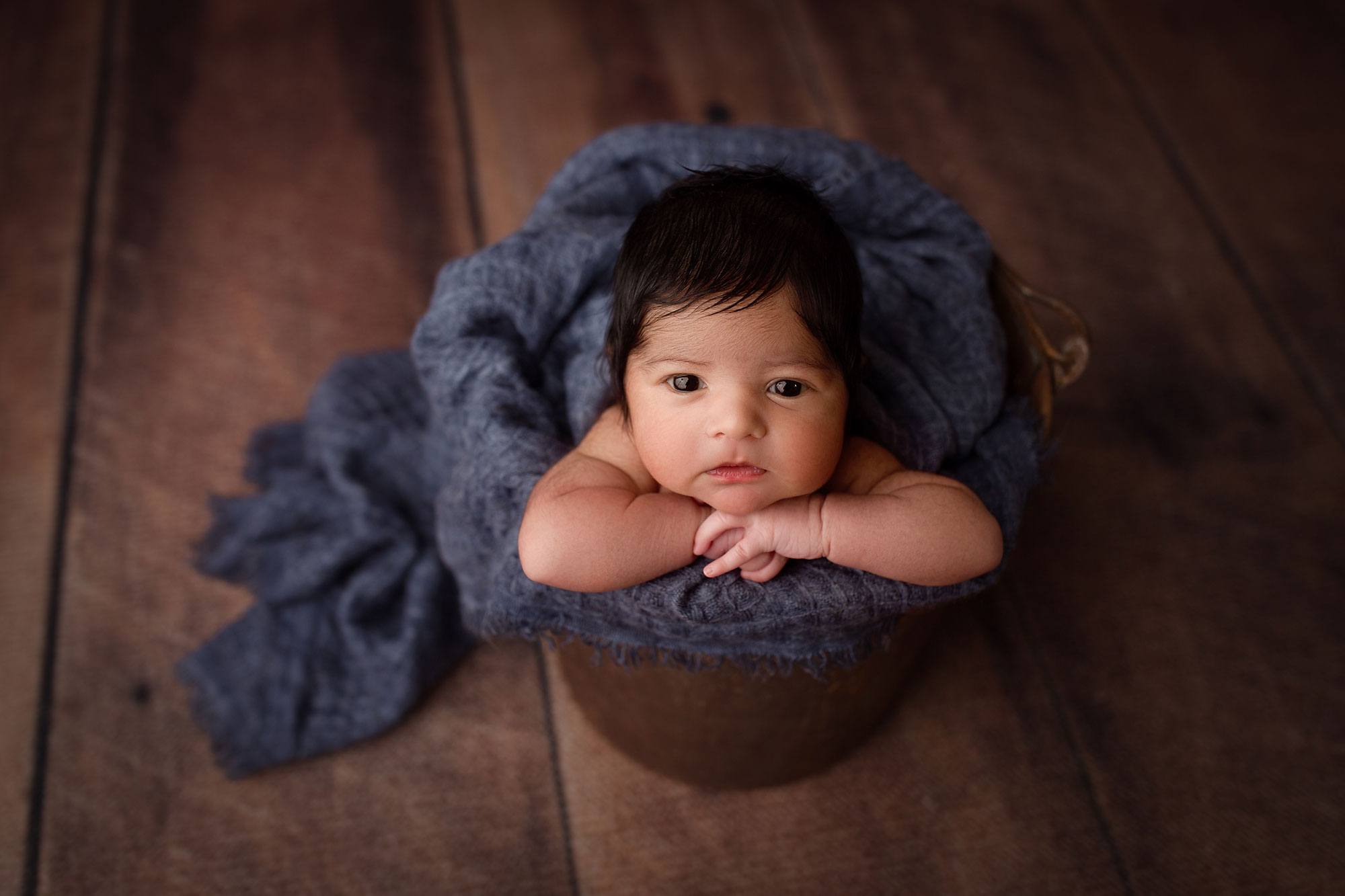 new jersey newborn images, baby sitting up in bucket with hands under chin and wrapped in blue blanket