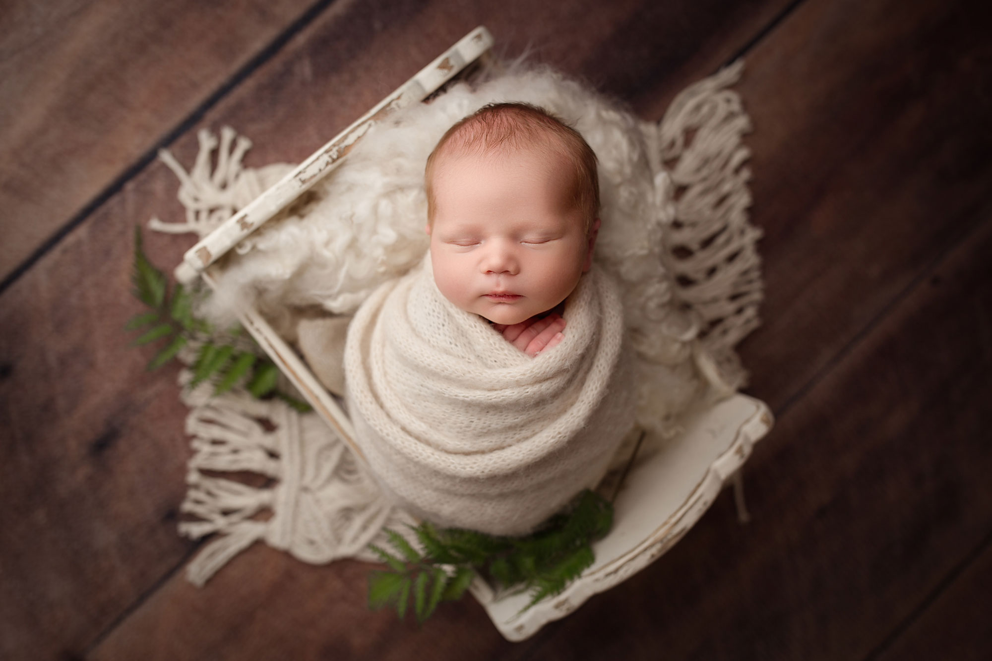 nj newborn photographer, swaddled baby asleep in tiny distressed wooden bed with blankets and greenery