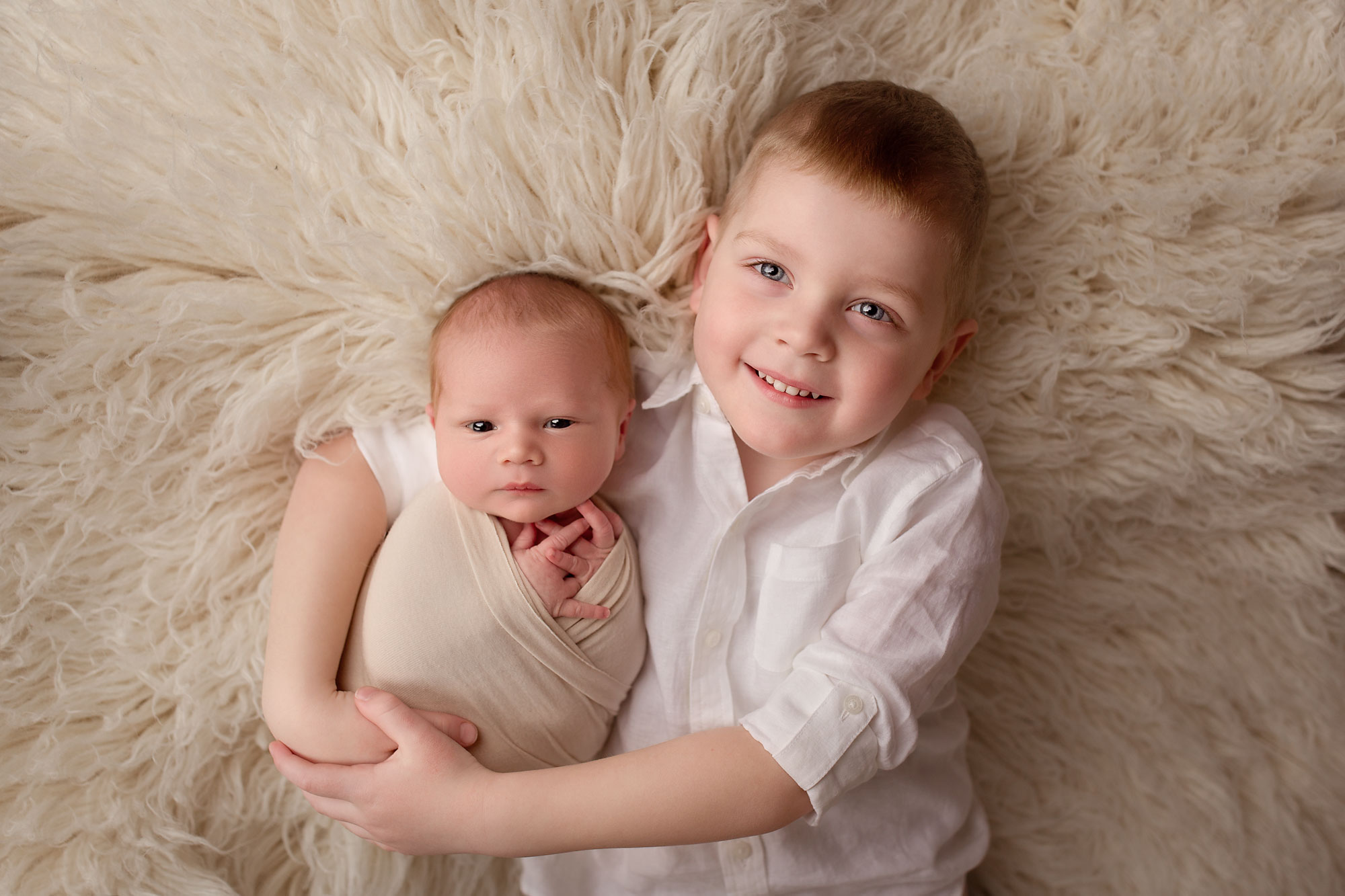 baby and sibling photos, big brother and infant baby lying on cream fur rug together