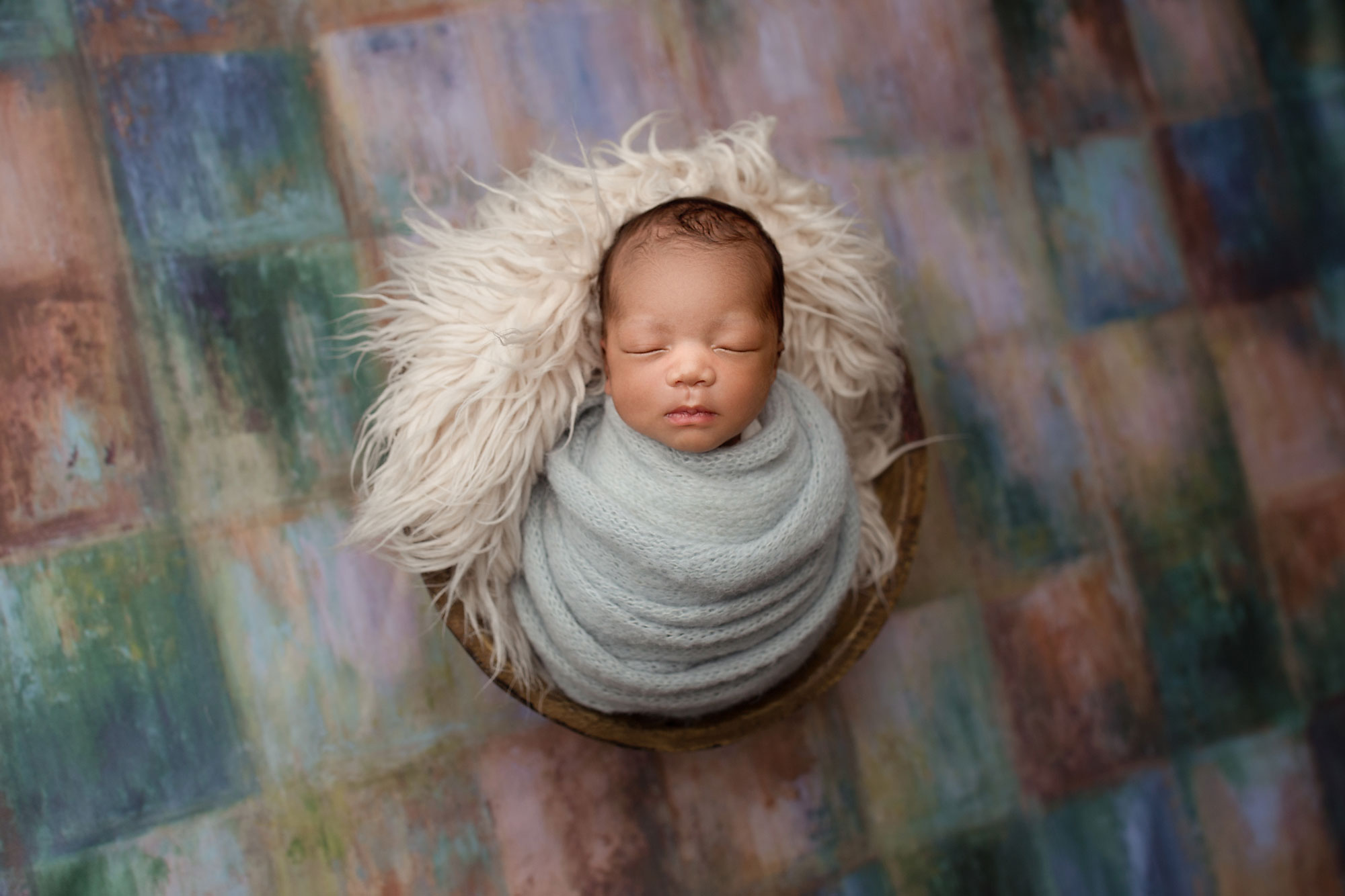 beautiful newborn pictures nj, swaddled baby asleep in bucket against colorful backdrop