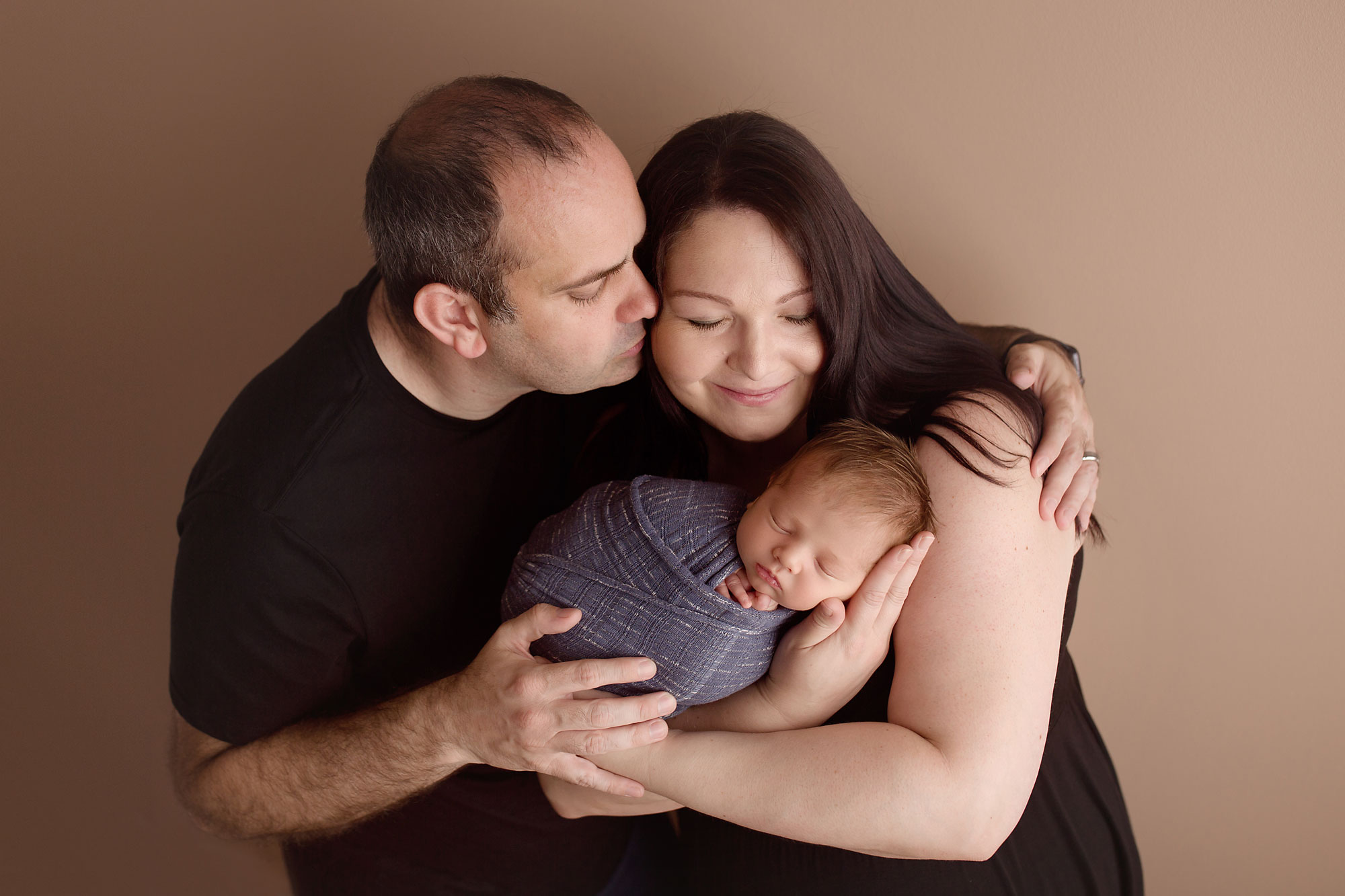 family photo session near me nj, dad kissing mom while they hold new baby