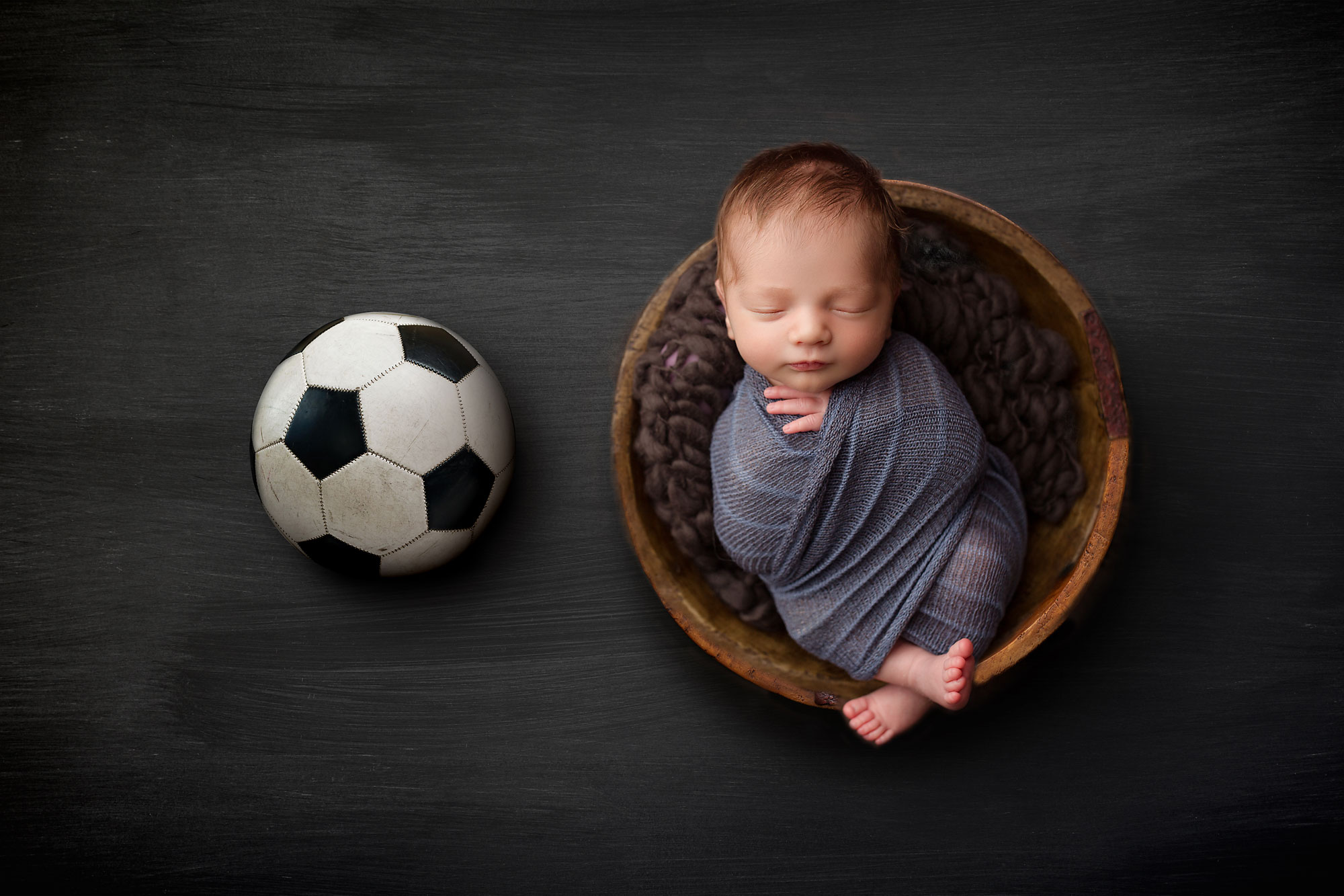 newborn pictures hunterdon county, baby boy sleeping in bowl against gray backdrop with soccer ball