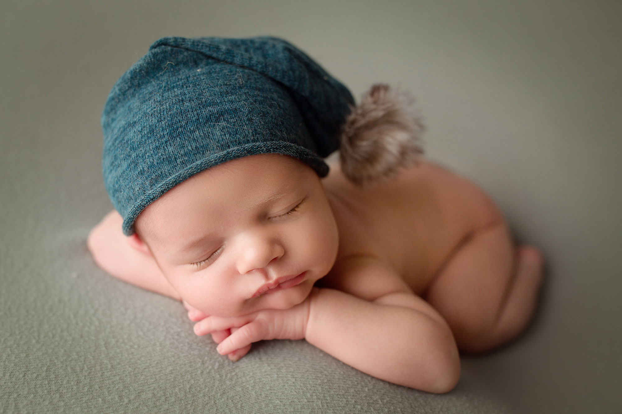 newborn photographer monmouth county, baby boy asleep on gray background in blue cap