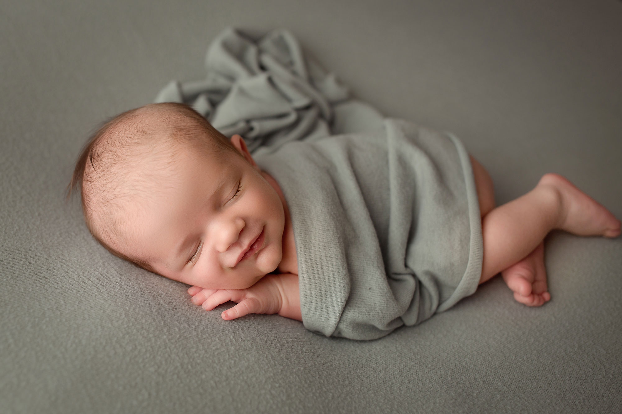 newborn baby photographer, baby asleep and smiling wrapped in gray blanket