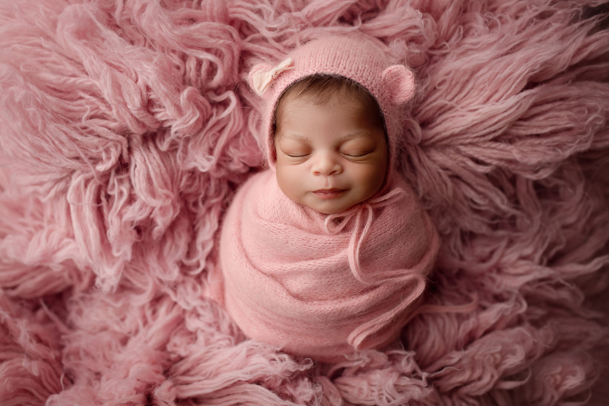 newborn photos woodbridge nj, smiling baby girl asleep in pink swaddle and bear hat with bow