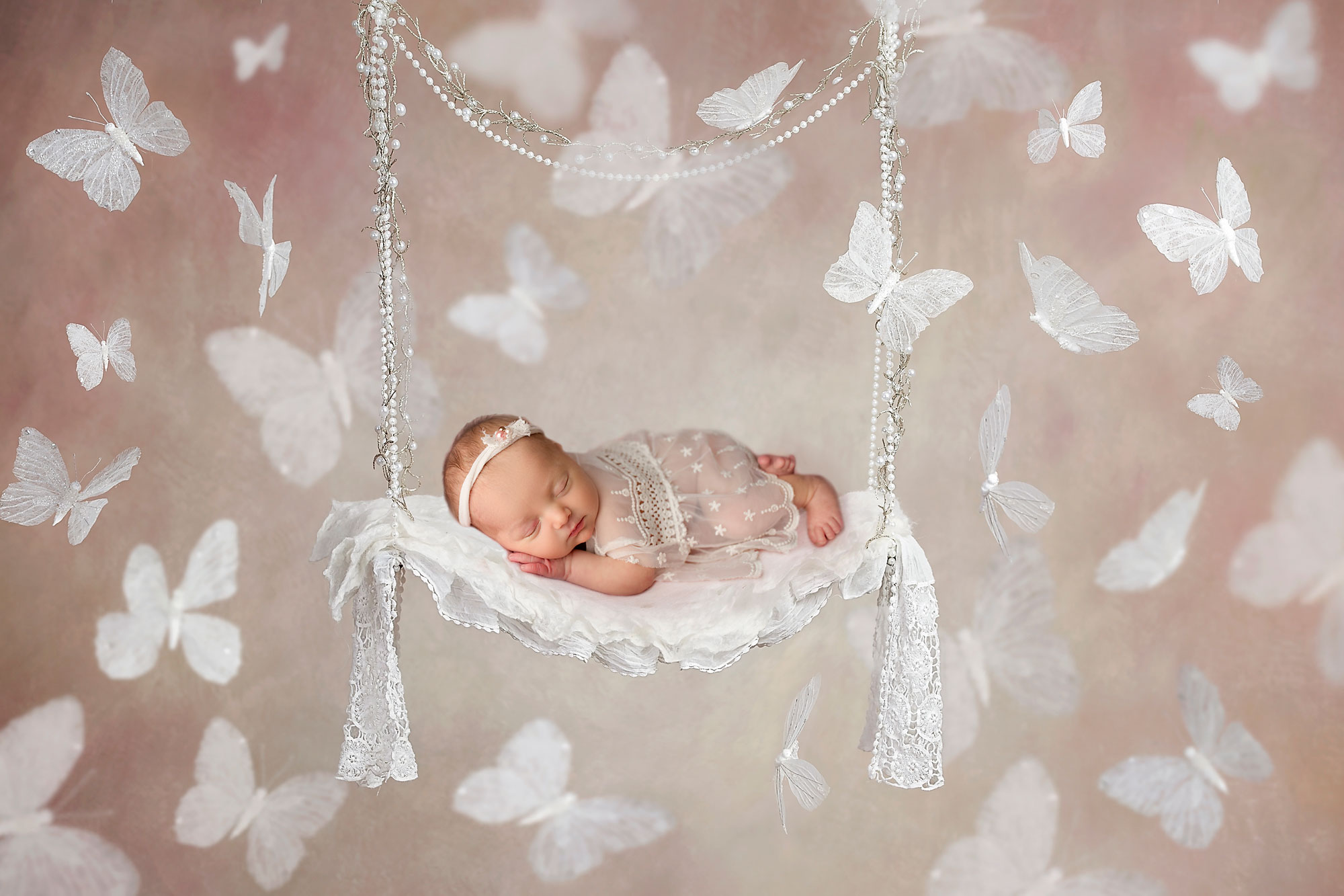 Creative photographs of newborn babies butterflies white and baby sleeping in a white swing surrounded by white butterflies 