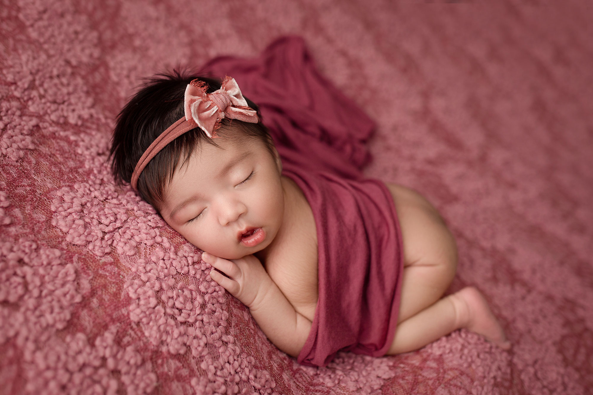 newborn images, baby girl on textured pink backdrop with bow in hair