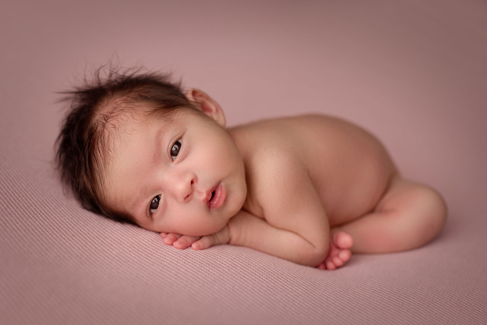 awake baby girl newborn photography session posed beanbag pose on a pink blanket 