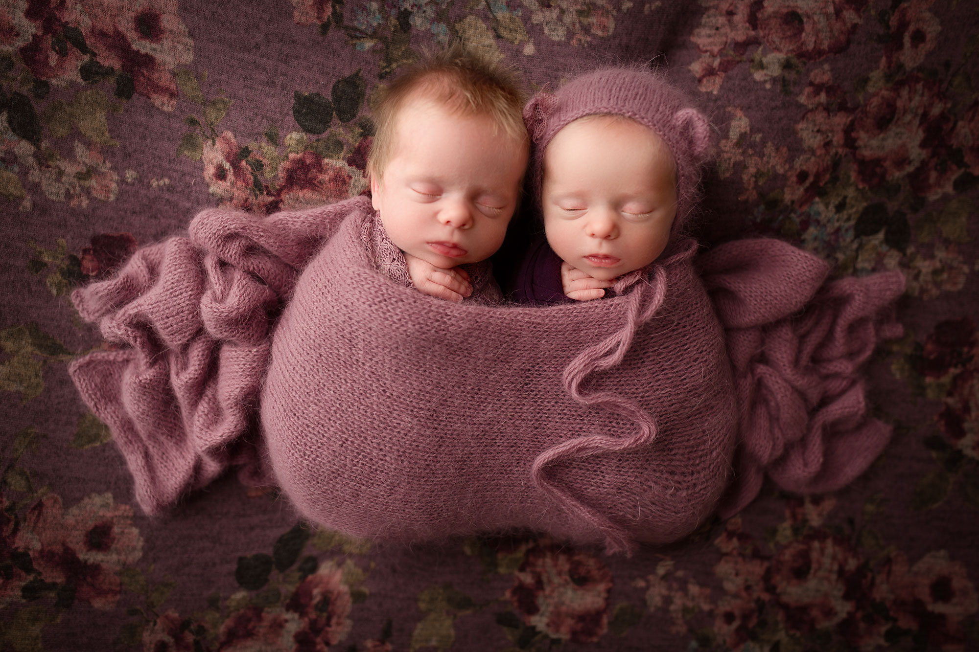twin girls snuggling together on a purple blanket 