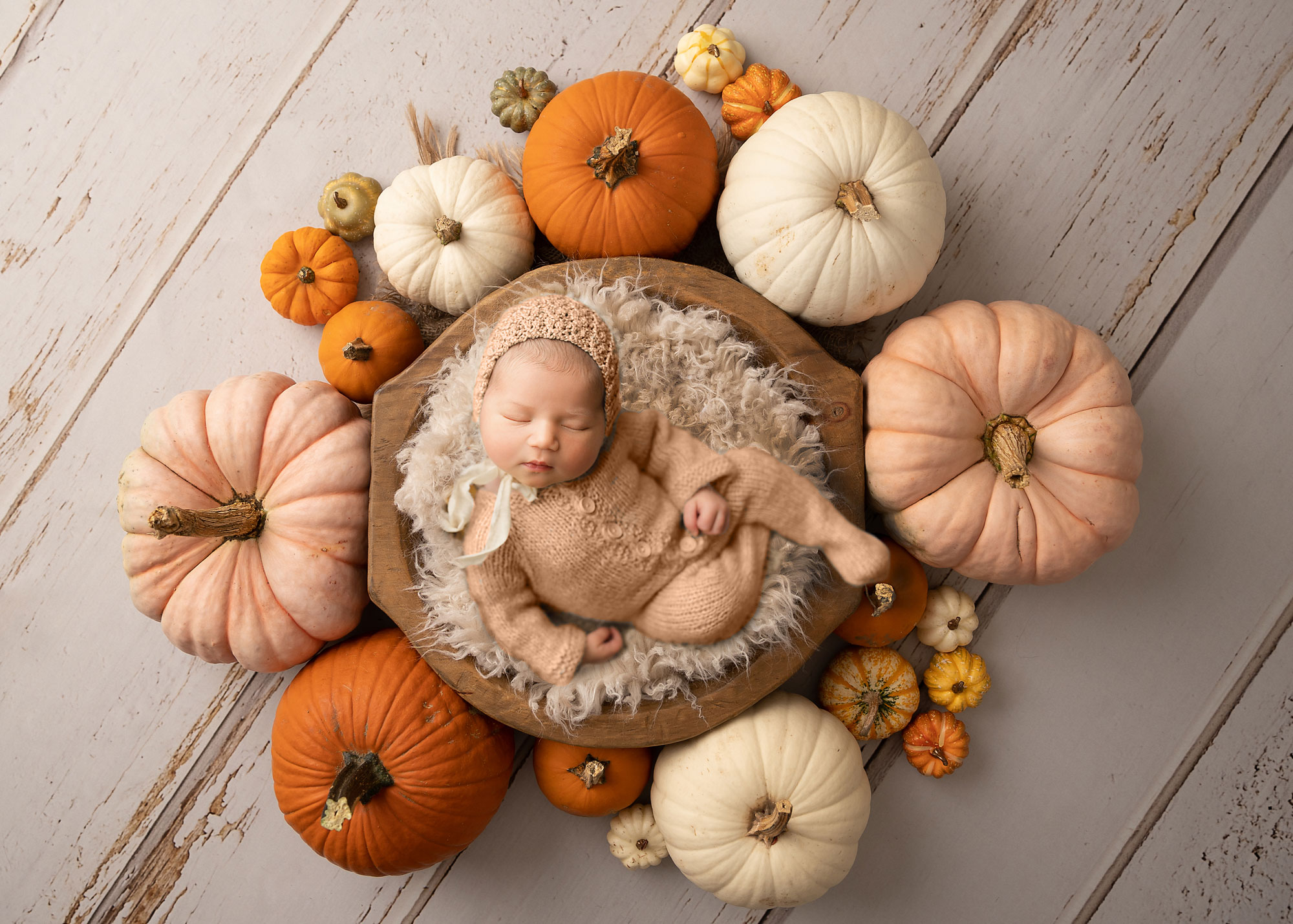 baby girl sleeping in a basket with many pumpkins around 