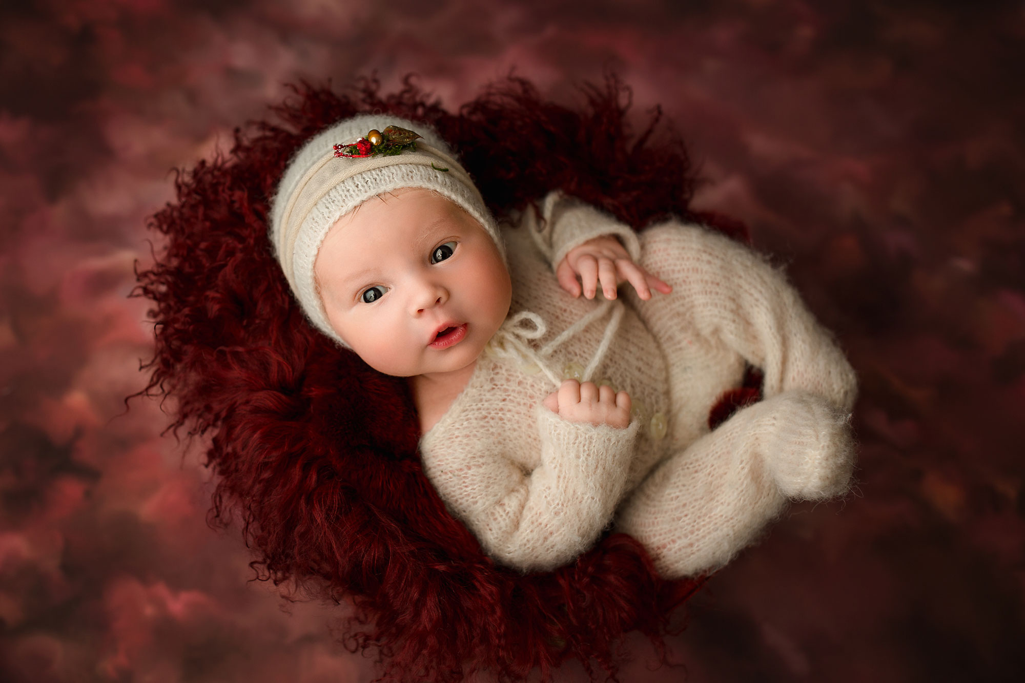 newborn baby girl in a cream christmas set up on a red backdrop
